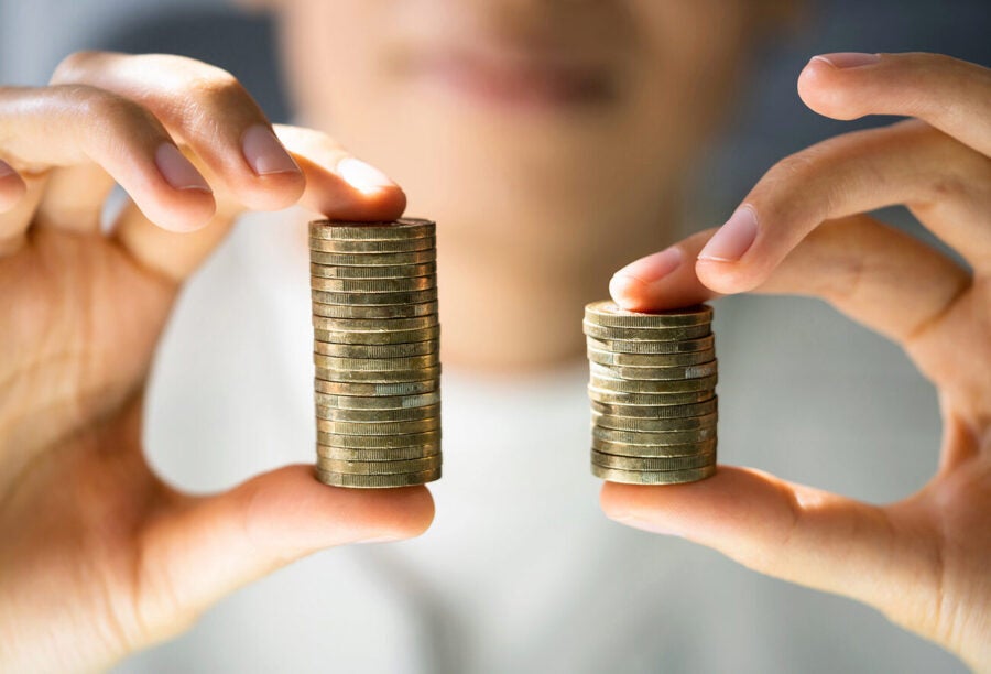 Person holding up two uneven stacks of coins to show how income inequality in America is hurting our collective happiness